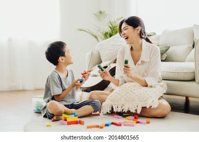 Cute Asian woman and kid playing educational toys together in living room. Mom and son play cubes and laugh Happy family. Young mother and son doing activities together at home.