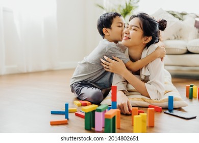 Cute Asian Woman And Kid Playing Educational Toys Together In Living Room. Boy Hugs His Mom With Love. Happy Family. Young Mother And Son Doing Activities Together At Home.