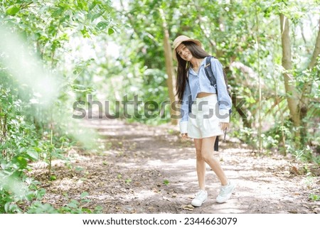 Cute Asian woman with long hair wearing hat walking in community forest, park which is a rural nature education center. relax and relieve the exhaustion from working all week during the long weekend.