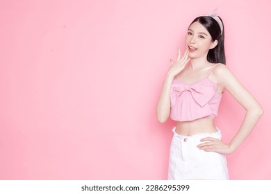 Cute Asian woman model gathered in ponytail with korean makeup style on face have plump lips and clean fresh skin wearing pink camisole open mouth announcement on isolated pink background.