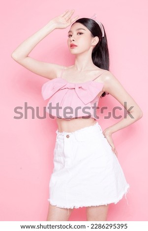 Cute Asian woman model gathered in ponytail with korean makeup style on face have plump lips and clean fresh skin wearing pink camisole Raise her hand to cover the sun on isolated pink background.