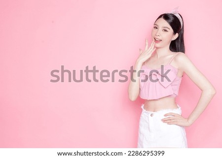 Cute Asian woman model gathered in ponytail with korean makeup style on face have plump lips and clean fresh skin wearing pink camisole open mouth announcement on isolated pink background.