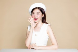 Cute Asian Woman With Perfect Skin And Screaming Announcement. Pretty Girl Model Wearing White Beret And Natural Makeup On Beige Background. Cosmetology, Beauty And Spa, Wellness, Plastic Surgery.