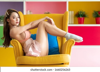 Cute Asian Woman Sitting On Yellow Arm Chair. Sexy Pose. For Seductive Sensuality And Provocative Desire Concept.