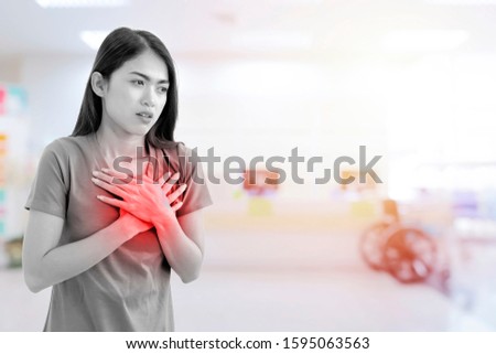 A cute Asian woman is suffering from acute heart disease, showing signs of illness by using her hands to hold her chest. Hospital background, Black and white image with red graphics