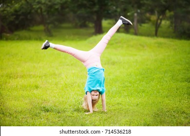 Cute Athletic Schooler Girl  Tumbling, Turning, Turn Handsprings In The Park. Sunny Summer Day. Sport For Children. Kid Doing Gymnastic And Having Fun. Healty Body. 
	
