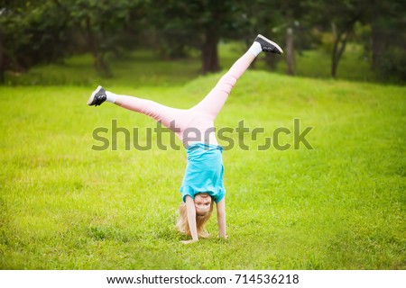 Cute athletic schooler girl  tumbling, turning, turn handsprings in the park. Sunny summer day. Sport for children. Kid doing gymnastic and having fun. Healty body. 
	
