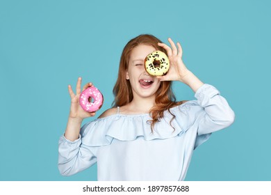 cute attractive child girl holding yummy donut and having fun isolated over blue background. Shows tongue.