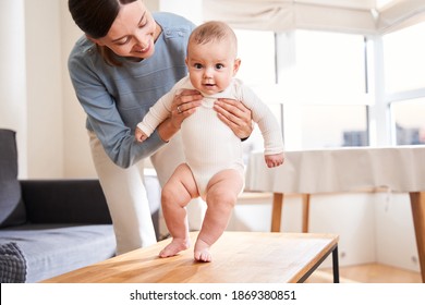 Cute attractive newborn baby taking first steps with lovely mother's help at home. Happy childhood and motherhood concept. Stock photo