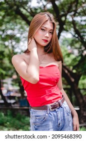 A cute and attractive southeast asian woman in a vivid red strapless top. Outdoor nature park scene. - Shutterstock ID 2095468390