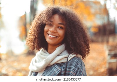 Cute Autumn Close Up Portrait Of Young Smiling Happy African American Woman With Curly Hair Enjoying Walk In Park In Fall Season. Outdoor Photo Of Pleased Black Girl With Eyes In Love With Life