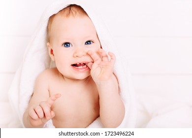 Cute Baby Of 8 Months In A Big White Towel Is Dressed On His Head. Holds Fingers In The Mouth. Clean Little Baby After Bath.