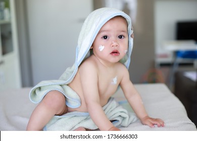 Cute Baby Applying Lotion Cream On Face And Body To Protect Skin After Bathing.mixed Race Asian-German Infant Wearing Green Towel Drying After Bath.adorable Child Sitting At Home.