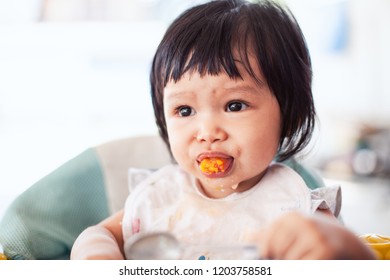 Cute Baby Asian Child Girl Eating Healthy Food By Herself And Making A Mess On Her Face And Hand