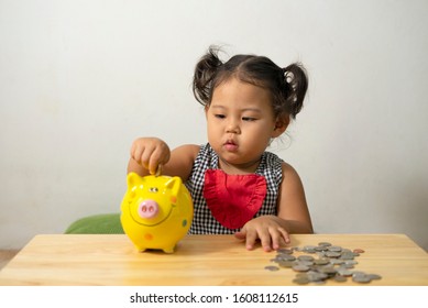 Cute Baby Asian Girl Playing With Coins Trying To Put Coins In Piggy Money Box. Baby Enjoy Learning How To Save Up Money. Concept Learning Financial Responsibility And Planning Saving Up Money.