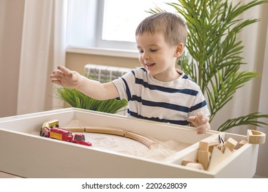 Cute Baby Boy Confident Playing Railroad Train Toy On Wooden Sand Table Therapy Childish Early Development. Preschooler Male Kid Play Cars Playthings Railway. Fine Motor Skills Home Leisure Activity