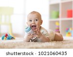 Cute baby boy drinking from bottle. Kid lying on carpet in nursery at home. Smiling child is 7 months old.