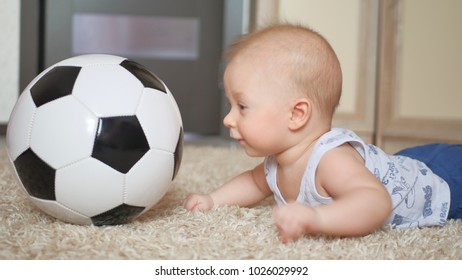 cute baby boy with football ball lying on the floor in the children's room.
