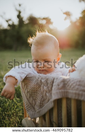 Cute baby boy and his toy playing in a wooden box making funny and happy faces warm summer sunset in the park 
