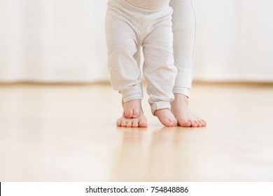Cute baby boy learning to walk and make his first steps. mom is holding his hand. child's feet close up, copy space