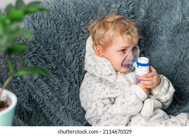 Cute Baby Boy Makes Inhalation With A Nebulizer Equipment. Sick Child Holding Inhalator In Hand And Breathes Through An Inhaler At Home. Physical Therapy For Cold, Flu And Bronchial Asthma