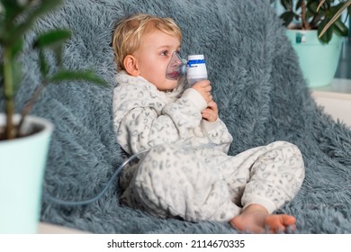 Cute Baby Boy Makes Inhalation With A Nebulizer Equipment. Sick Child Holding Inhalator In Hand And Breathes Through An Inhaler At Home. Physical Therapy For Cold, Flu And Bronchial Asthma