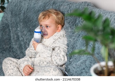 Cute Baby Boy Makes Inhalation With A Nebulizer Equipment. Sick Child Holding Inhalator In Hand And Breathes Through An Inhaler At Home. Physical Therapy For Cold, Flu And Bronchial Asthma