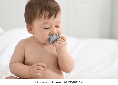 Cute baby boy with pacifier on bed at home