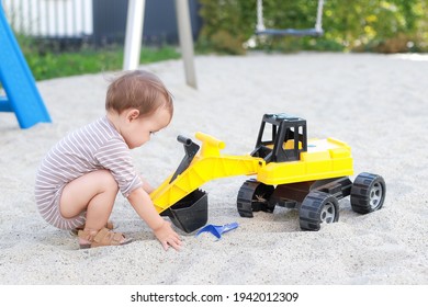 Cute Baby Boy Playing With Excavator, Truck Toys On Playground. Little Child Having Fun On Sand The Summer. Kid Play With Toy Car Outdoor Background. Mixed Race Asian-German