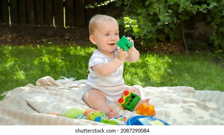 Cute baby boy playing with toys on grass at house backyard. Concept of child development, education and relaxing outdoors.