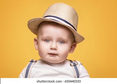 Cute baby boy posing in summer hat on yellow background. Adorable little child in studio.