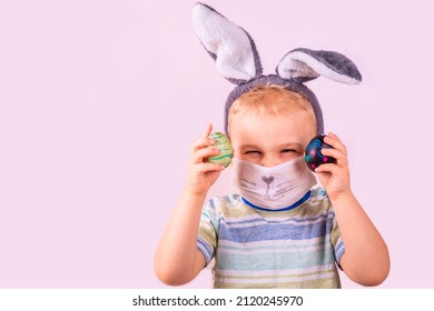 Cute Baby Boy In Rabbit Bunny Ears On Head And Protective Mask With Colored Eggs On Pink Background. Cheerful Smiling Happy Child. Covid Easter Holiday Banner