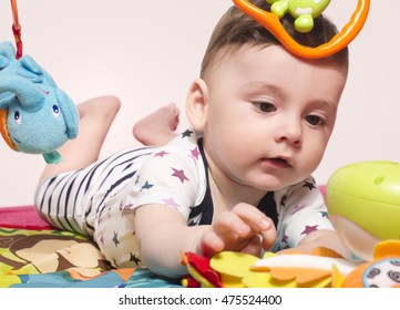 Cute Baby Boy Sitting On A Playmat And Playing With Toys. Adorable Six Month Old Child Happy Crawling To Reach The Toys.