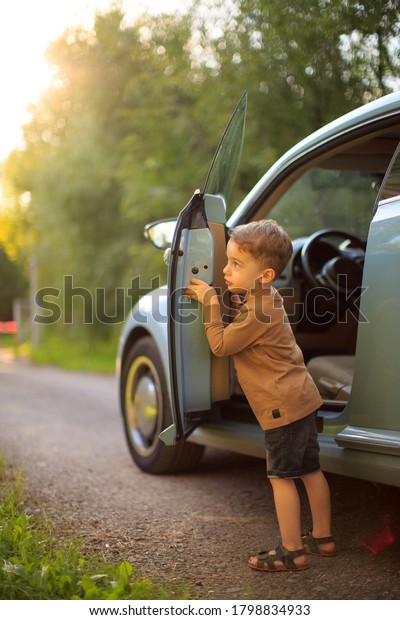Cute baby\
boy small driver standing near the car in sunlight. Summertime\
photography for ad or blog about family\
trip