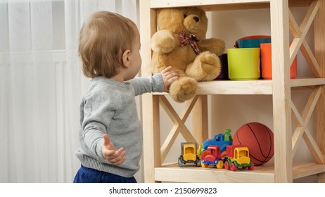 Cute baby boy taking teddy bear toy from bookshelf in playroom. Child education. - Shutterstock ID 2150699823