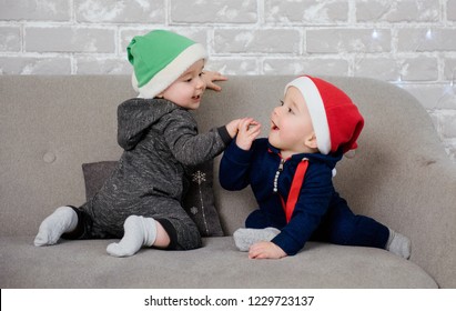 Cute baby boy twins wearing Santa hats and playing with each other on the sofa. Winter holidays magic and sweet family memories