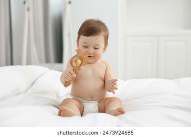 Cute baby boy with wooden rattle on bed at home - Powered by Shutterstock