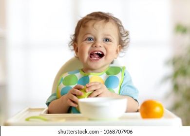 Cute Baby Child Eating Healthy Food. Portrait Of Happy Kid Boy With Bib In High Chair.