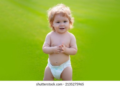 Cute Baby In Diaper On Green Grass In Summertime. Funny Little Kid On Nature. Happy Childhood. Baby And Summer Sunny Weather. Funny Little Child Closeup Portrait. Kids Emotion, Happy Smiling Face.