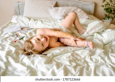 Cute Baby Draws With A Marker On A White Bed. Smeared Hands And Feet, Dirty In Paint. Funny Picture, Funny Kid.