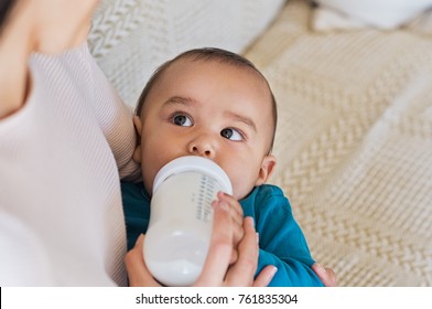 Cute Baby Drinking Milk From Baby Bottle While Looking His Mom. Mother Feeding Son Infant From Bottle. Little Boy Drinking Milk From Bottle At Home.