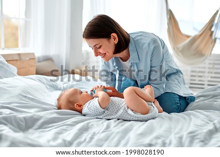 Cute baby drinking milk from baby bottle while looking his mom. Mother feeding son infant from bottle. Little boy drinking milk from bottle at home.