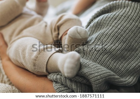 Cute baby feet in beige socks, child with mother on bed, happy motherhood