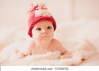 Cute baby girl 2-3 months old wearing red knitted hat crawling in bed closeup. Childhood.