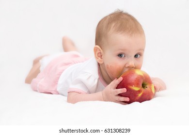 A Cute Baby Girl With A Dermatitis On Her Cheeks Is Eating A Red Apple On An Isolated White Background. Food Allergy