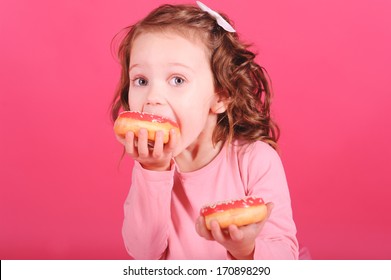 Cute baby girl eating sweet donuts over pink background