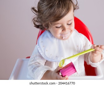 Cute baby girl eating yogurt smiling. Her pretty face has yogurt around her mouth.