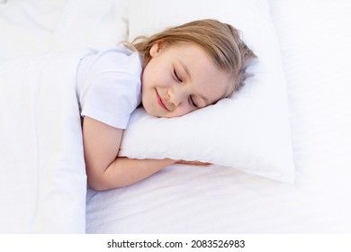 A Cute Baby Girl Hugs A Pillow With Her Hands Folded Under Her Cheek And Sleeps On The Bed On A White Cotton Bed Under A Blanket, A Healthy Baby's Sleep At Night