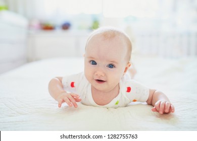 Cute baby girl lying on her tummy on bed. Happy healthy kid in nursery