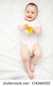 Cute Baby Girl Playing With Rattle On Bed. Top View